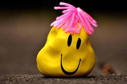 Climate anxiety_Depressed yellow smiley face with pink yarn hair on a dark surface.