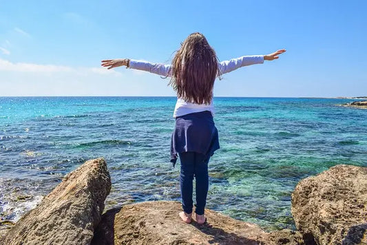 Woman standing on rock with arms outstretched 